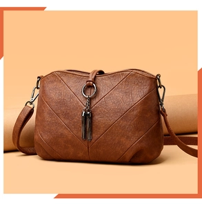 Détail d'un sac bandoulière marron foncé avec coutures en V et ornements à franges
