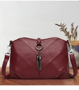 Détail de sac bandoulière en cuir bordeaux avec surpiqûres en V et doubles glands