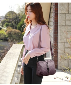 Photo de mode en extérieur montrant un sac bandoulière violet grainé avec pompon en cuir