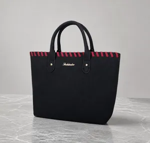 Detail of black tote bag with red-black braided trim and gold metal rivets on surface