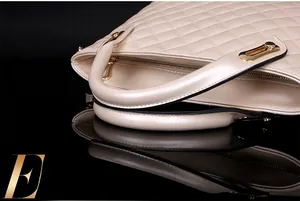 Close-up of quilted beige handbag featuring gold zipper and elegant curved handle