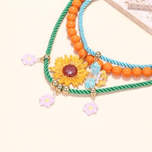Dettaglio della collana a più strati con girasole smaltato, farfalla blu e ciondoli a margherita