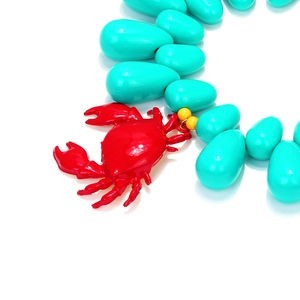 Detail of red enamel crab pendant and blue turquoise-style beads for summer necklace
