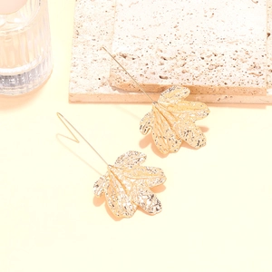 Macro detail of gold leaf pendant earrings with textured finish on stone surface