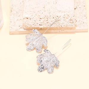 Detailed view of silver leaf-shaped earrings with textured finish on natural travertine