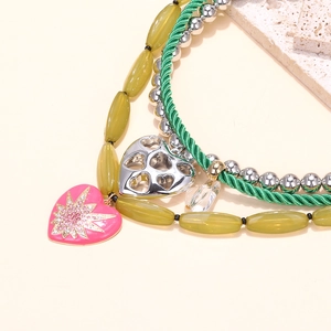 Detail of multi-layered necklace featuring pink enamel heart and green beaded chain strands
