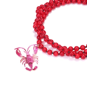 Detail of creative triple-strand red beaded necklace with a pink lobster pendant