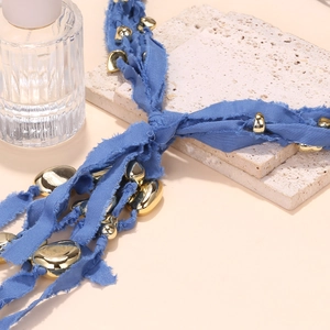 Detail of blue frayed fabric necklace with irregular golden beads on textured stone