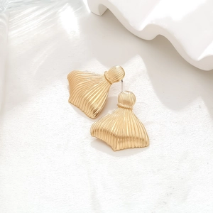 Detailed view of golden fishtail earrings with vertical striped texture on white stand