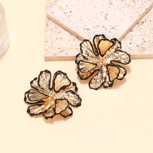 Detail of oversized gold flower earrings with black enamel edges and brushed metal texture