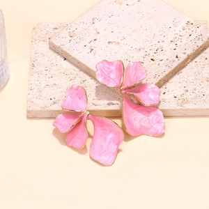 Dettaglio di orecchini a fiore in smalto rosa con bordi dorati su pietra beige