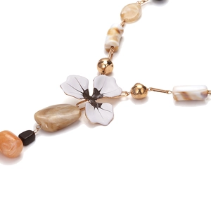 Détail du pendentif fleur en émail blanc et des perles en résine marbrée sur le collier