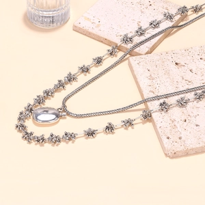 Détail de colliers superposés argentés avec chaîne florale et pendentif ovale poli