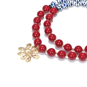 Macro view of multi-layer beaded necklace with red pearls and golden evil eye palm pendant