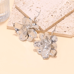 Close-up of oversized silver metal flower earrings with detailed textured petals