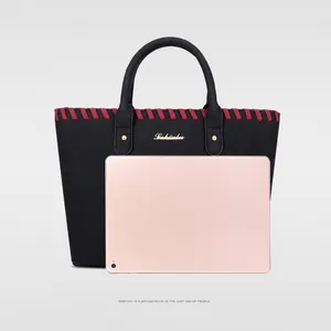 Detailed view of black tote bag size comparison with tablet showing red woven trim and rivets