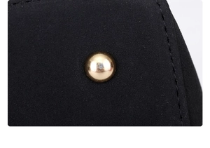 Macro shot of black suede bag featuring polished gold metal stud and detailed stitching