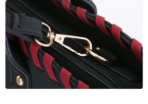 Detail of golden hardware lobster clasp with red woven trim on black crossbody bag