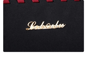 Detailed close-up of golden metal logo on black suede leather bag with red woven edge