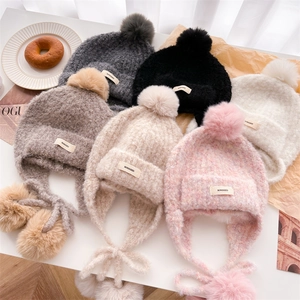 Flat lay of colorful knit balaclava hats with plush pompoms and warm ear flaps