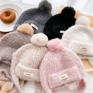 Detailed knit texture of solid color balaclava hats with fluffy pom-poms and brand label