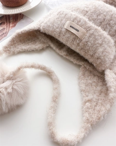 Detail of beige fleece balaclava with soft earflaps and plush pom-pom decoration