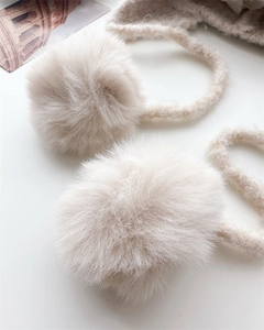 Detailed macro view of soft cream faux fur pom-poms and chunky knit strap of balaclava