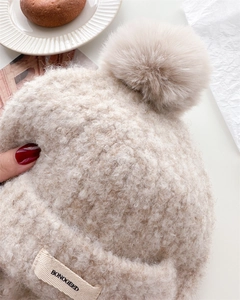 Detail of beige fleece balaclava beanie with fluffy pompom and stitched brand label