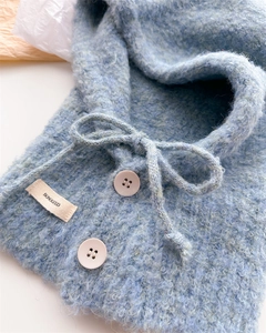 Dettaglio del passamontagna in lana azzurro con trama a maglia, cordoncino e bottoni rosa