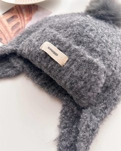 Close-up of grey curly lamb wool balaclava with fluffy pompom and branded woven label
