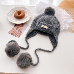 Close-up of dark grey knitted Balaclava with fluffy pom-poms and minimalist logo tag