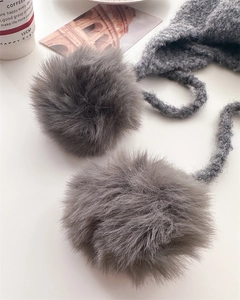 Detail of grey knitted balaclava showing fluffy oversized pom-poms and textured rope tie