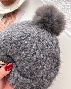 Detail of grey wool balaclava featuring a fluffy pompom and soft bouclé knit texture