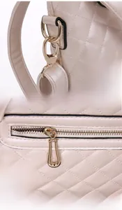 Detail view of gold hardware hooks and smooth zipper on a beige quilted handbag