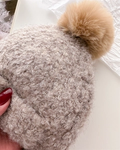 Detail of soft beige knit balaclava hat featuring a large fluffy brown pom-pom texture