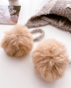 Close-up of beige knitted balaclava hat with fluffy dual pom-poms and warm ear flaps