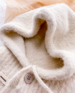 Dettaglio del passamontagna in pile bianco con coulisse e chiusura con bottone marrone