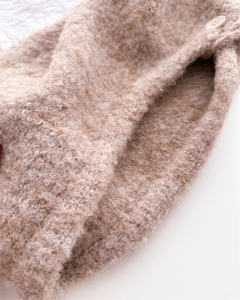 Dettaglio della maglia bouclé color avena con bottone su un caldo passamontagna invernale