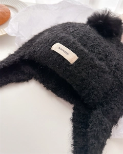 Detail of black curly knit balaclava hat with large pompom and woven brand label