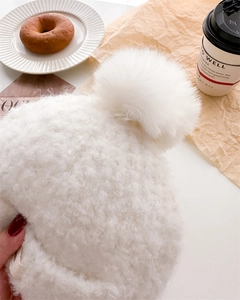 Close-up of a white knit balaclava hat with fluffy pom-pom and soft wool texture