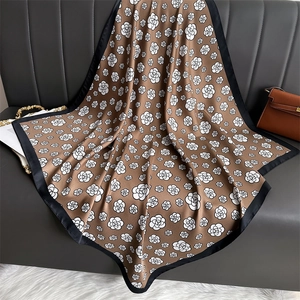 Vintage silk-feel square scarf with camellia floral print and black border on leather couch