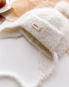 Detail of white knit balaclava hat with fluffy pom-pom and branded woven label tag