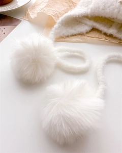 Detail of soft white wool balaclava featuring fluffy fur pom-poms on a cozy background
