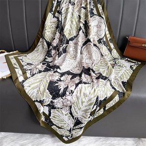 Carré de soie satiné aux motifs floraux olive et beige posé sur un canapé chic