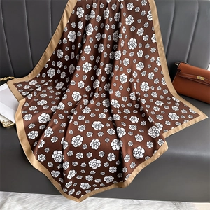Detailed drape of a silk-textured brown scarf with white floral patterns on a leather sofa