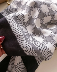 Dettaglio di un foulard in seta con bordi neri e motivi a catena H geometrici