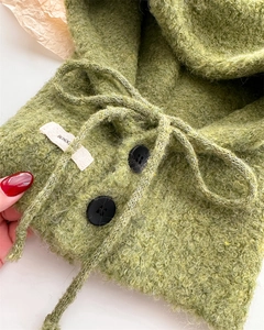 Dettaglio passamontagna verde in maglia con trama in pile, bottoni neri e coulisse regolabile
