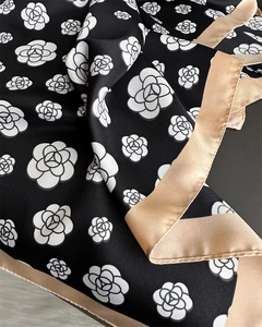 Macro detail of twill silk scarf showing white camellia floral print and champagne border