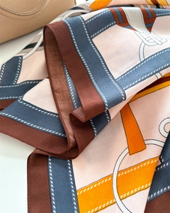 Detailansicht eines Seidenschals mit Trensen- und Kettenmustern auf einer Ledertasche