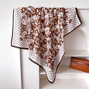 Close-up of silk-feel scarf draped on a rack showing rose floral print and polka dots